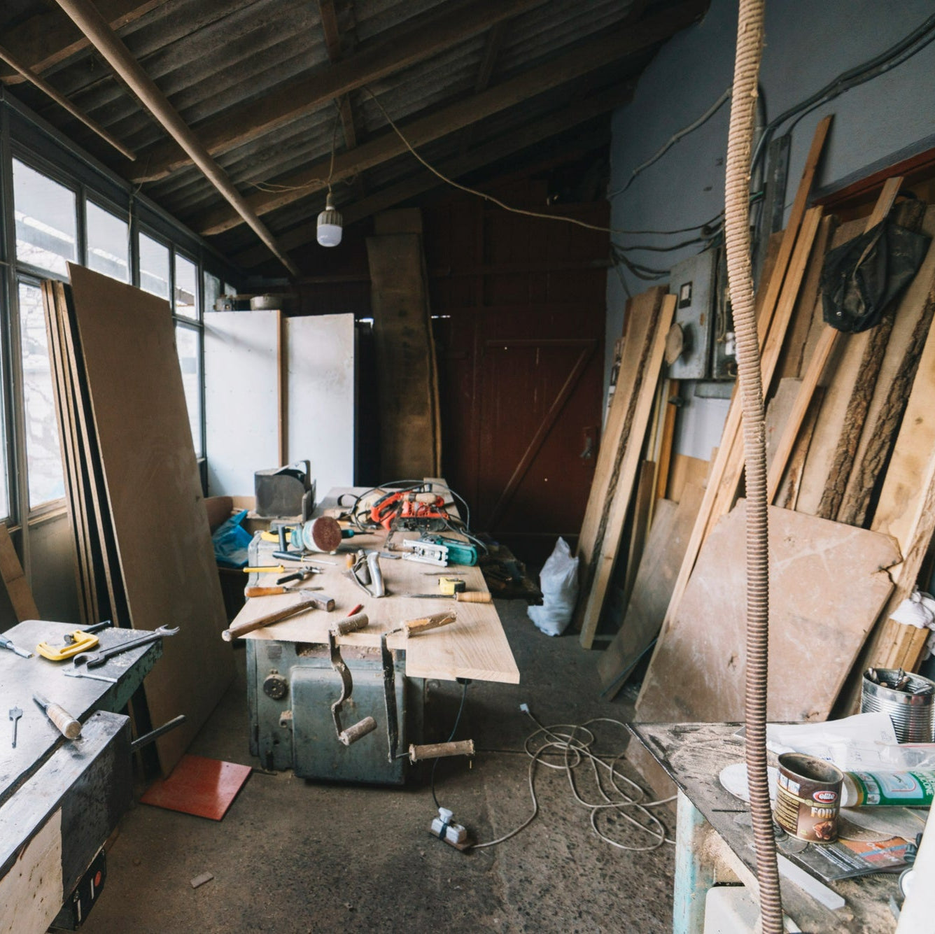 Workshop with tools and materials on a table, large windows, and wooden planks.