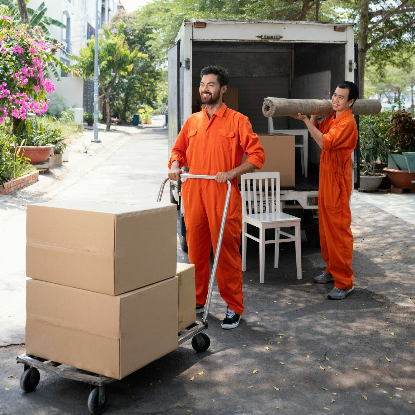 Two men in orange uniforms with moving boxes and furniture outside a truck.