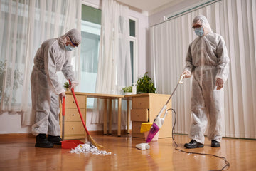 Two people in protective suits cleaning a room with a broom and vacuum.